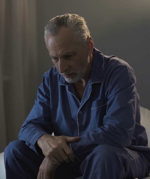 Senior man in pajamas sitting up in bed needing insomnia treatment in Dallas