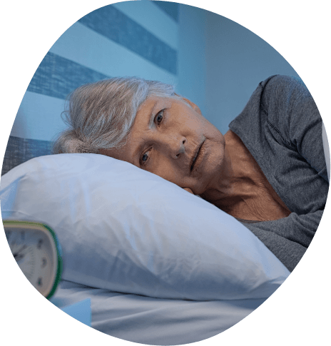 Older woman lying in bed staring at alarm clock on bedside table
