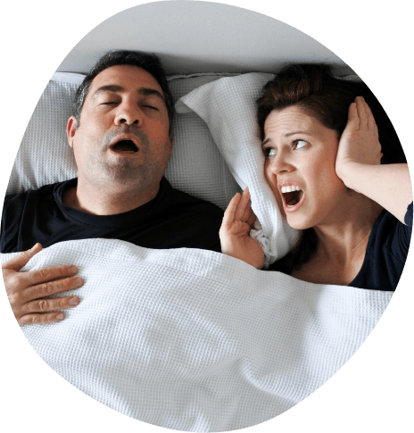 Woman in bed covering ears with pillow next to snoring man